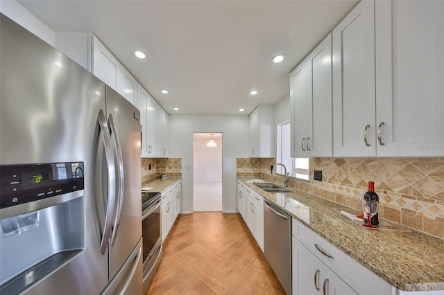 kitchen featuring sink, white cabinetry, stainless steel appliances, light stone counters, and light parquet flooring