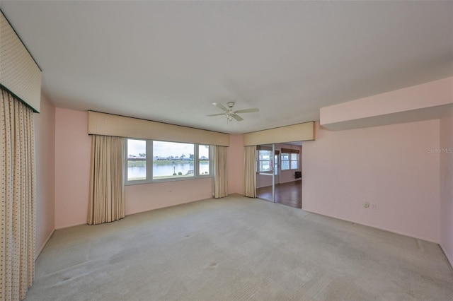 carpeted spare room with a water view and ceiling fan