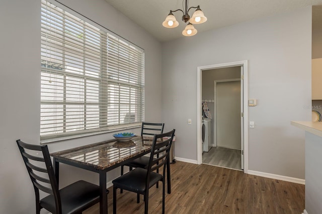 dining room featuring washer / dryer, dark wood finished floors, baseboards, and an inviting chandelier