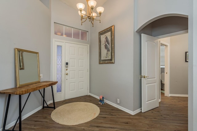 entrance foyer featuring arched walkways, dark wood-style flooring, a notable chandelier, and baseboards