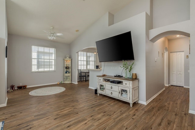 living area with arched walkways, dark wood-style flooring, a ceiling fan, and baseboards