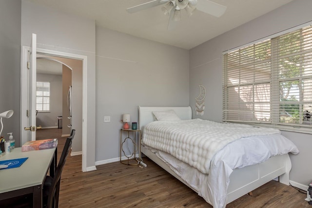 bedroom with dark wood-type flooring, arched walkways, ceiling fan, and baseboards