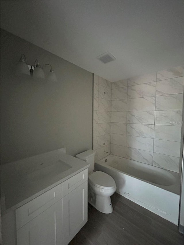 full bathroom with wood-type flooring, tiled shower / bath, vanity, and toilet