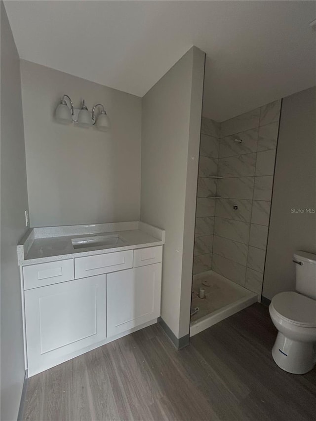 bathroom featuring vanity, toilet, hardwood / wood-style floors, and a tile shower