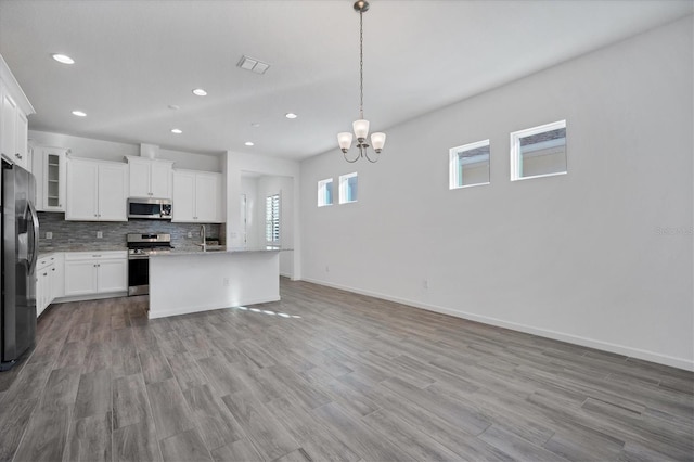 kitchen featuring a kitchen island with sink, hanging light fixtures, backsplash, stainless steel appliances, and white cabinets