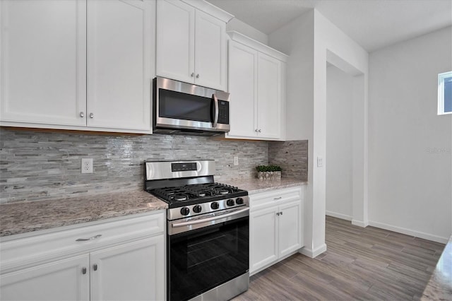 kitchen with white cabinetry, light stone countertops, light hardwood / wood-style flooring, and stainless steel appliances