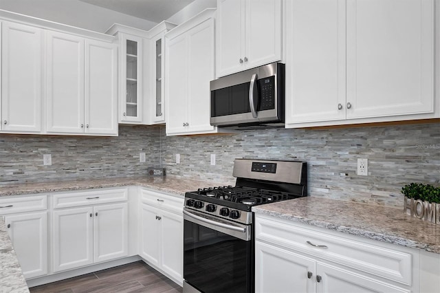 kitchen with white cabinetry, backsplash, light stone counters, and appliances with stainless steel finishes