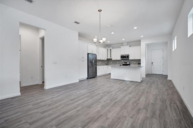 kitchen with white cabinetry, hanging light fixtures, stainless steel appliances, a kitchen island with sink, and backsplash