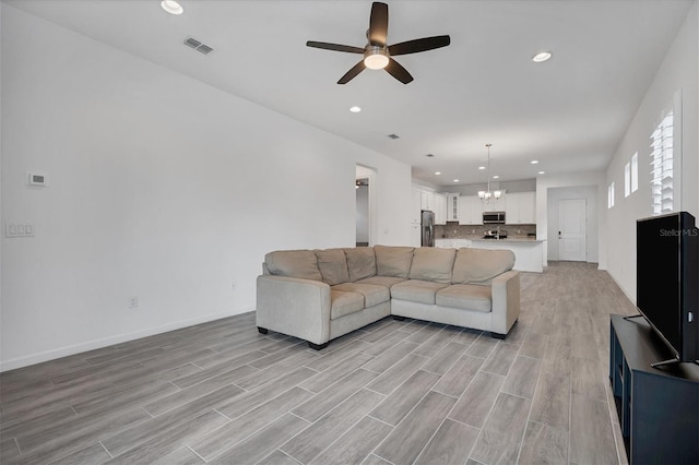 living room featuring ceiling fan with notable chandelier and light hardwood / wood-style flooring