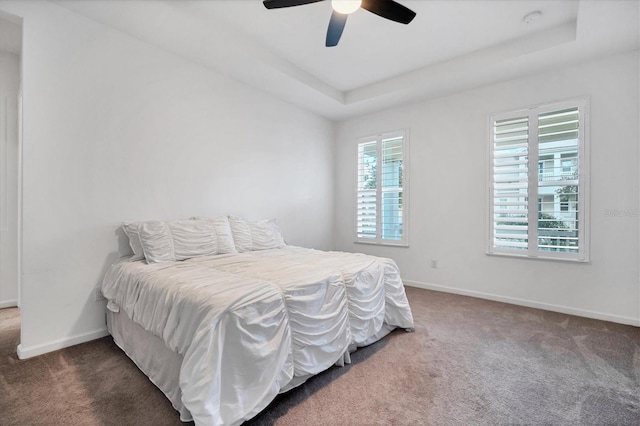 bedroom featuring a raised ceiling, ceiling fan, and dark carpet