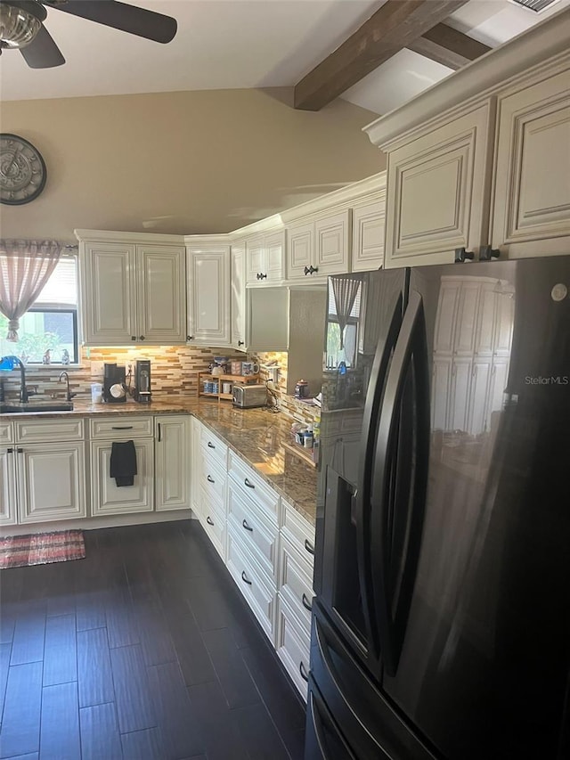 kitchen with sink, vaulted ceiling with beams, black fridge, light stone counters, and tasteful backsplash