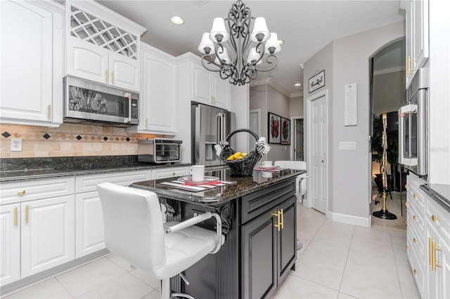 kitchen featuring white cabinetry, hanging light fixtures, stainless steel appliances, a center island, and dark stone counters