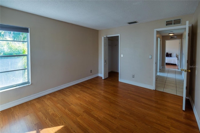 unfurnished bedroom featuring hardwood / wood-style flooring, a walk in closet, and a textured ceiling