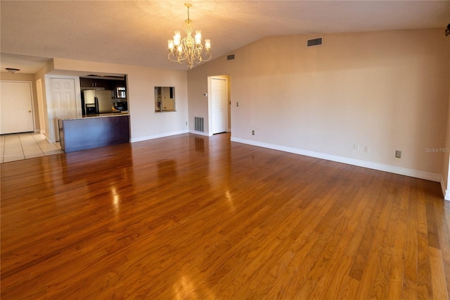 unfurnished living room featuring lofted ceiling, a chandelier, and light wood-type flooring