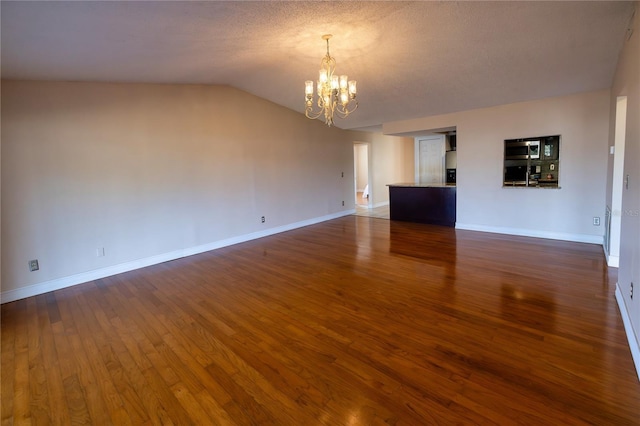 interior space with dark wood-type flooring, vaulted ceiling, an inviting chandelier, and a textured ceiling