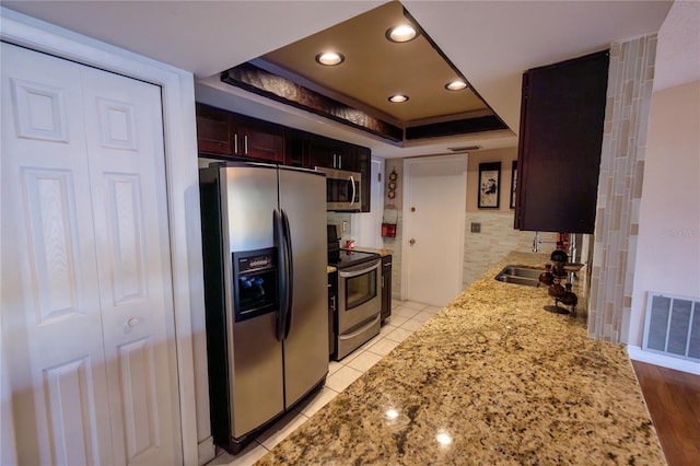 kitchen featuring sink, light tile patterned floors, a raised ceiling, stainless steel appliances, and light stone countertops