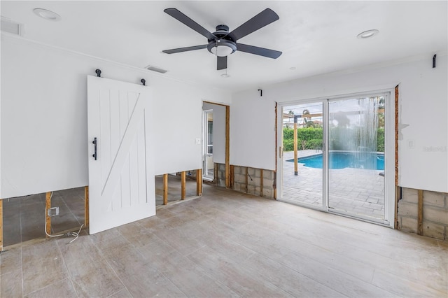 empty room featuring ceiling fan, ornamental molding, and a barn door