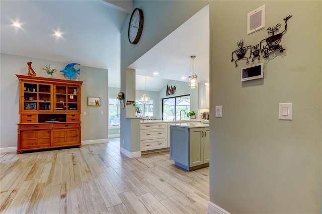 kitchen featuring sink, light hardwood / wood-style flooring, hanging light fixtures, kitchen peninsula, and white cabinets