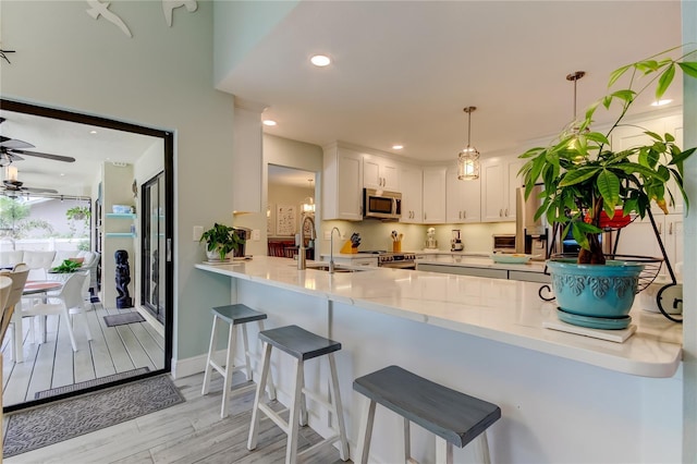 kitchen with ceiling fan, appliances with stainless steel finishes, white cabinetry, decorative light fixtures, and kitchen peninsula