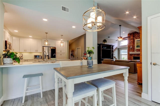 kitchen featuring white cabinets, hanging light fixtures, stainless steel appliances, a brick fireplace, and light hardwood / wood-style flooring