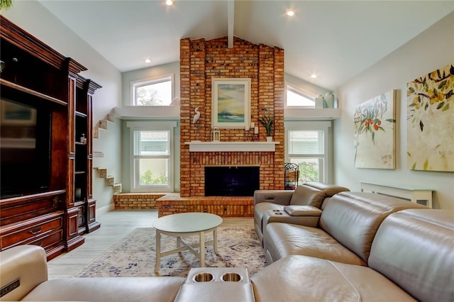 living room with a healthy amount of sunlight, light hardwood / wood-style floors, a brick fireplace, and vaulted ceiling with beams