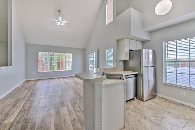 kitchen with sink, high vaulted ceiling, appliances with stainless steel finishes, kitchen peninsula, and white cabinets