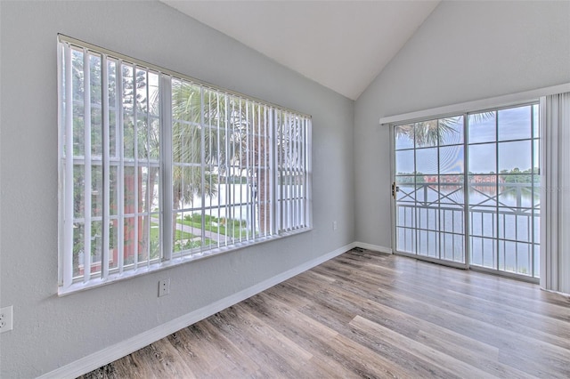 empty room featuring a water view, vaulted ceiling, and hardwood / wood-style floors