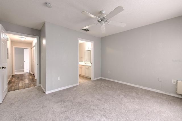 unfurnished bedroom with ceiling fan, light colored carpet, and ensuite bath