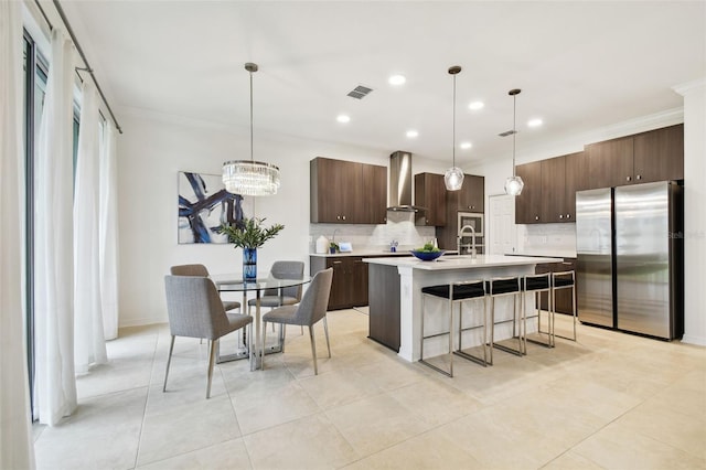 kitchen featuring dark brown cabinetry, visible vents, freestanding refrigerator, light countertops, and wall chimney range hood