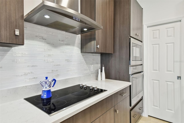 kitchen featuring dark brown cabinetry, decorative backsplash, wall chimney exhaust hood, light stone counters, and black electric cooktop