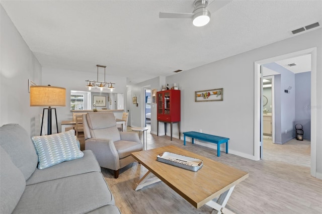 living room featuring ceiling fan, a textured ceiling, and light wood-type flooring