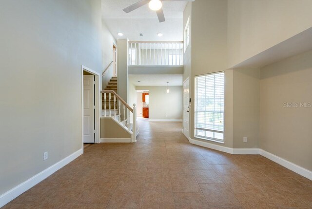 unfurnished living room featuring light tile patterned floors, a towering ceiling, and ceiling fan