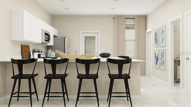 kitchen featuring stainless steel appliances, a kitchen breakfast bar, light tile patterned floors, and white cabinets