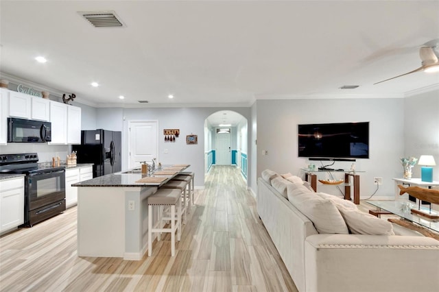 kitchen with a breakfast bar area, white cabinetry, dark stone countertops, black appliances, and a center island with sink