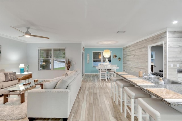 living room with sink, crown molding, light hardwood / wood-style floors, and ceiling fan