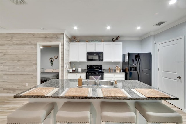 kitchen with stone counters, an island with sink, a kitchen bar, and black appliances