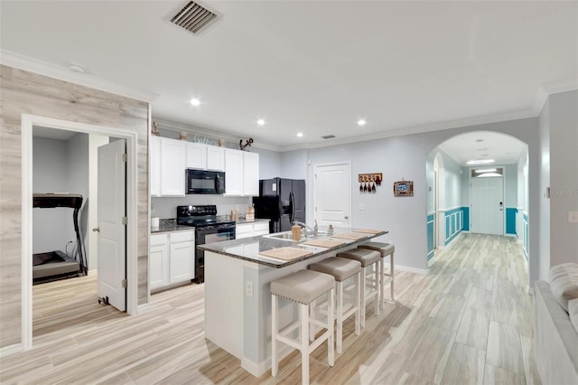 kitchen featuring white cabinetry, a kitchen bar, black appliances, a center island with sink, and light wood-type flooring