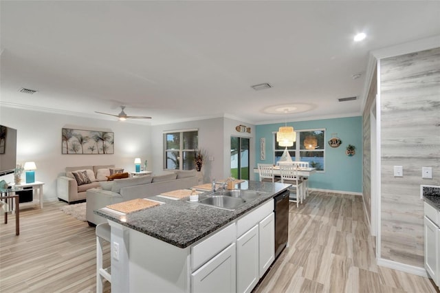 kitchen featuring sink, white cabinetry, crown molding, a center island with sink, and dark stone countertops