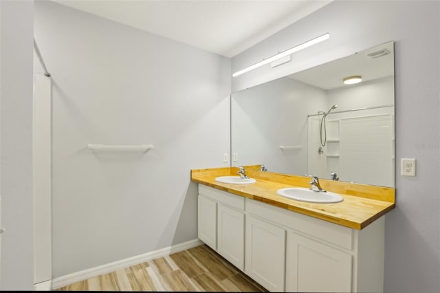 bathroom featuring walk in shower, wood finished floors, baseboards, and a sink