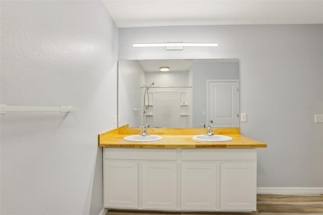 bathroom featuring double vanity, baseboards, a stall shower, and a sink