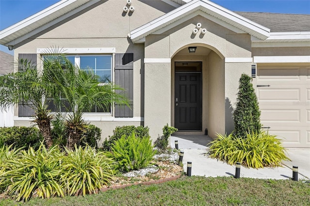 entrance to property with stucco siding, a garage, and a shingled roof