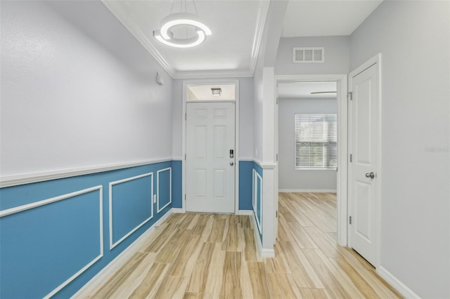 hallway featuring visible vents, ornamental molding, light wood-style floors, wainscoting, and a decorative wall