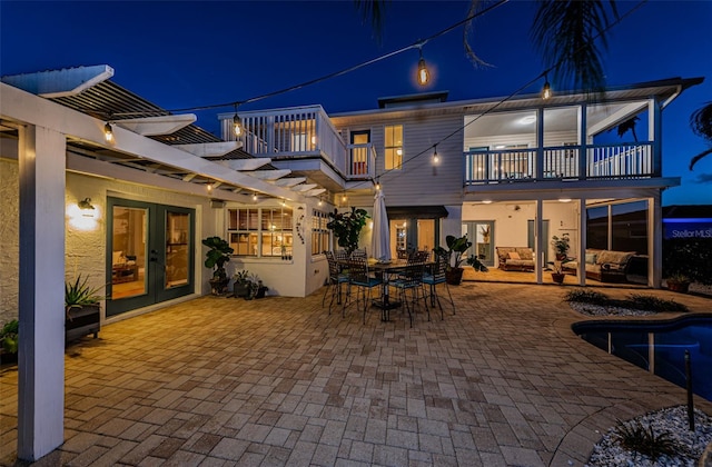 back house at night featuring a patio, a balcony, and french doors