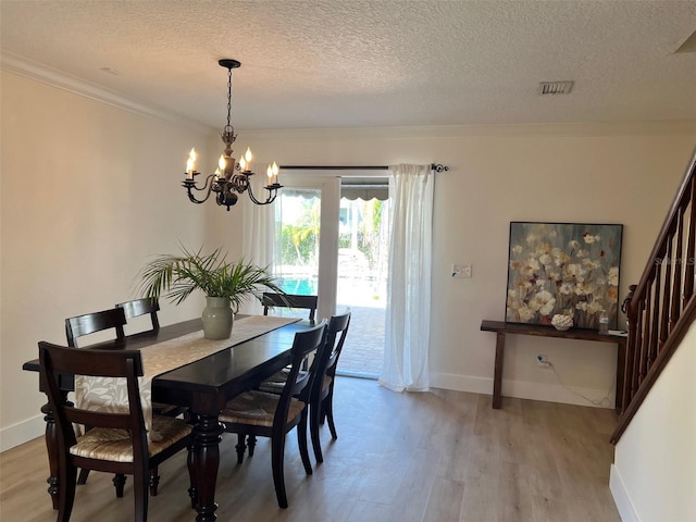 dining area with ornamental molding, an inviting chandelier, a textured ceiling, and light wood-type flooring