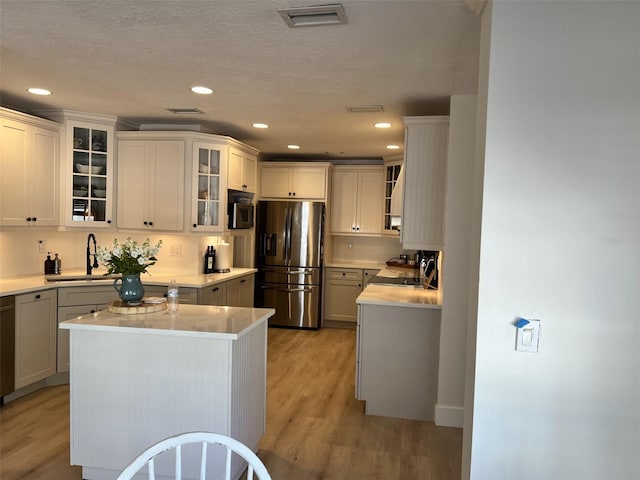 kitchen featuring appliances with stainless steel finishes, sink, white cabinets, a center island, and light wood-type flooring