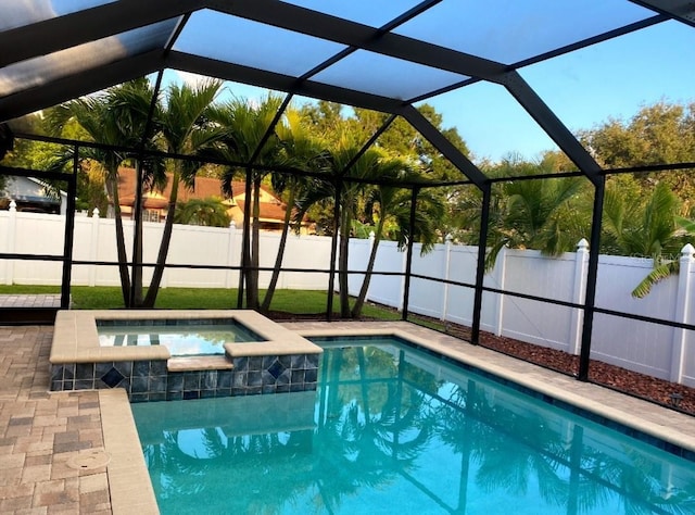 view of pool with a patio, glass enclosure, and an in ground hot tub