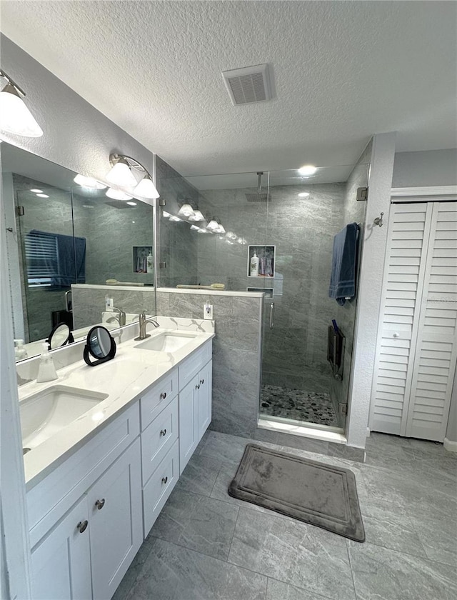 bathroom with vanity, a shower with shower door, and a textured ceiling