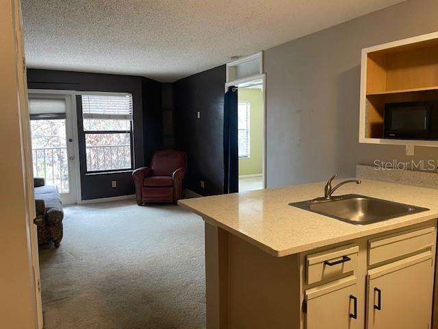 kitchen with sink, light colored carpet, kitchen peninsula, and a textured ceiling