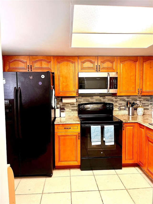 kitchen with light stone countertops, light tile patterned floors, backsplash, and black appliances