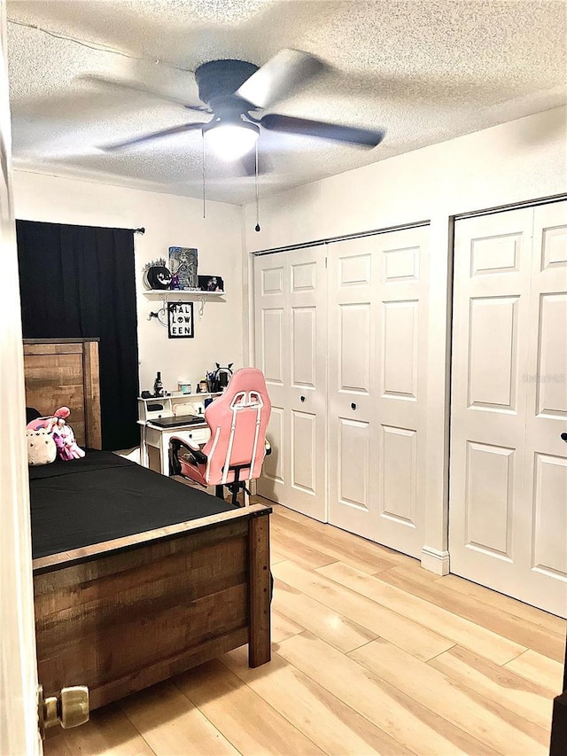 bedroom with hardwood / wood-style flooring, ceiling fan, two closets, and a textured ceiling